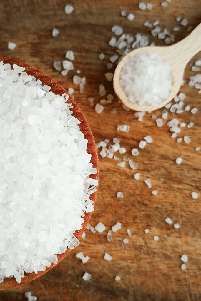 salt in a bowl with a wooden spoon of salt in the background