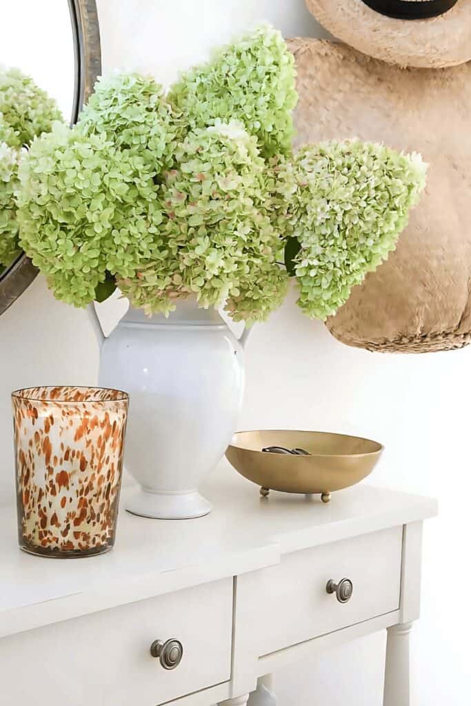 organized entry table with white vase of green hydrangeas, decorative bowl, and simple uncluttered styling
