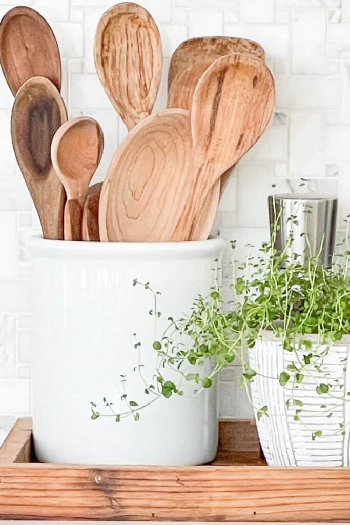 Wooden cooking utensils stored in a white crock with a small trailing plant for a simple, uncluttered kitchen look