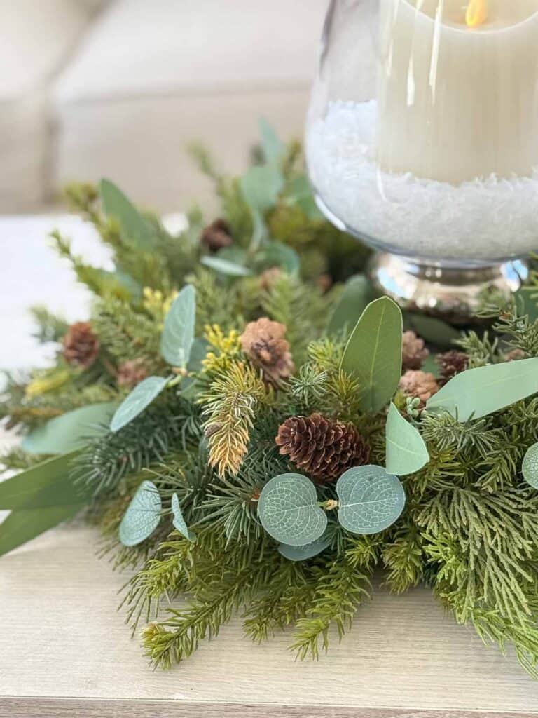 Christmas wreath used as a candle ring with faux evergreens, eucalyptus, and pinecones on a table