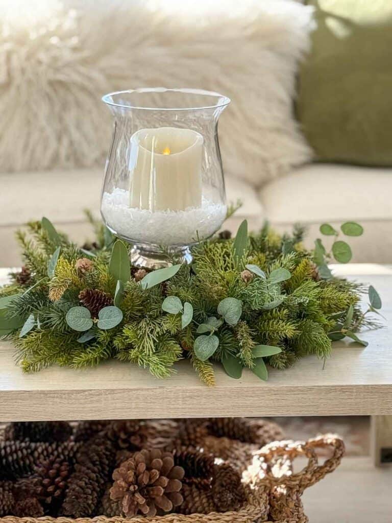 Christmas candle ring made with faux evergreens, eucalyptus, and pinecones on a coffee table