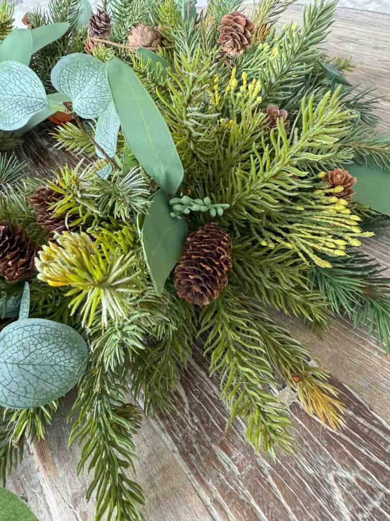 Close up of layered faux evergreen branches, pinecones, used to make a Christmas wreath