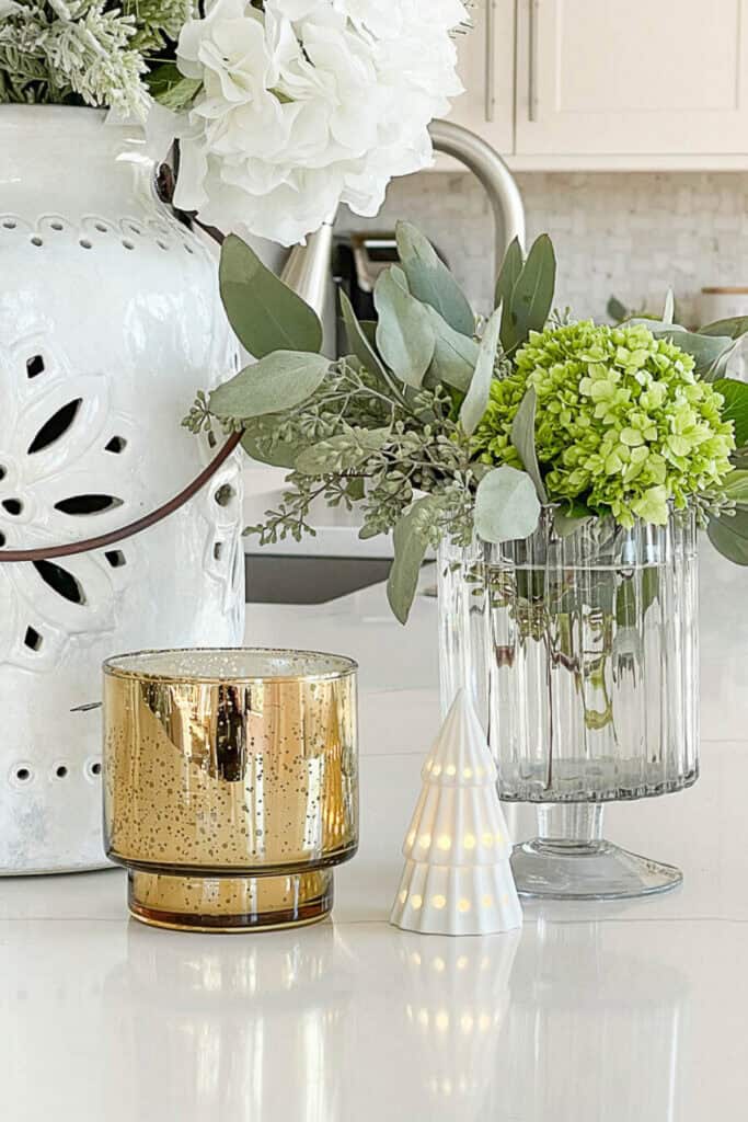 how to use faux Christmas greens on a kitchen counter with a vase of greens, a gold candle, and a white ceramic tree