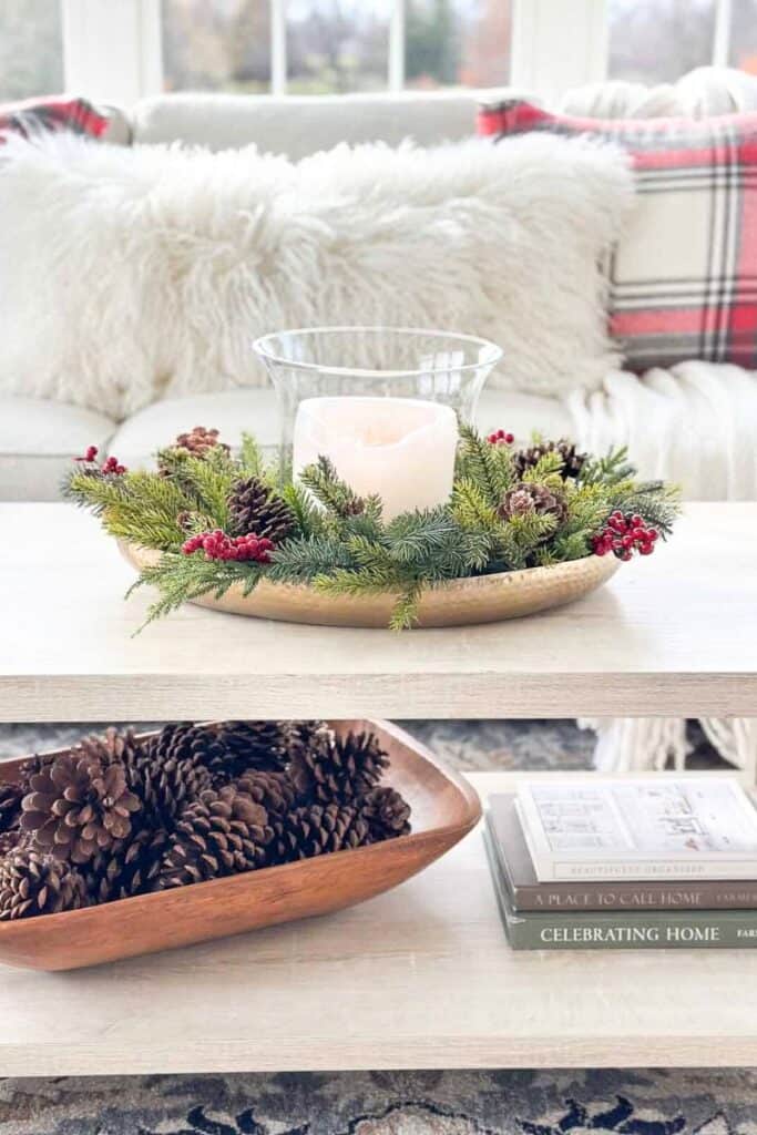 faux Christmas greens styled on a brass tray with a candle, pinecones, and red berries on a coffee table