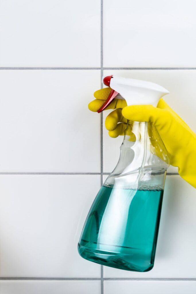 hydrogen peroxide in a glass spray bottle held by a woman in yellow cleaning gloves