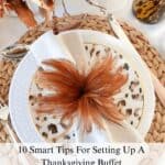 Beautiful Thanksgiving place setting with fall centerpiece and feather napkin accent. Learn 10 smart tips for setting up a Thanksgiving buffet.