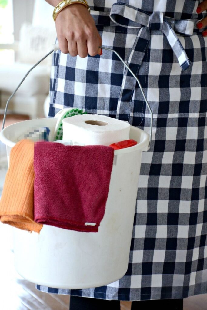 woman in an apron holding a bucket of natural cleaning supplies