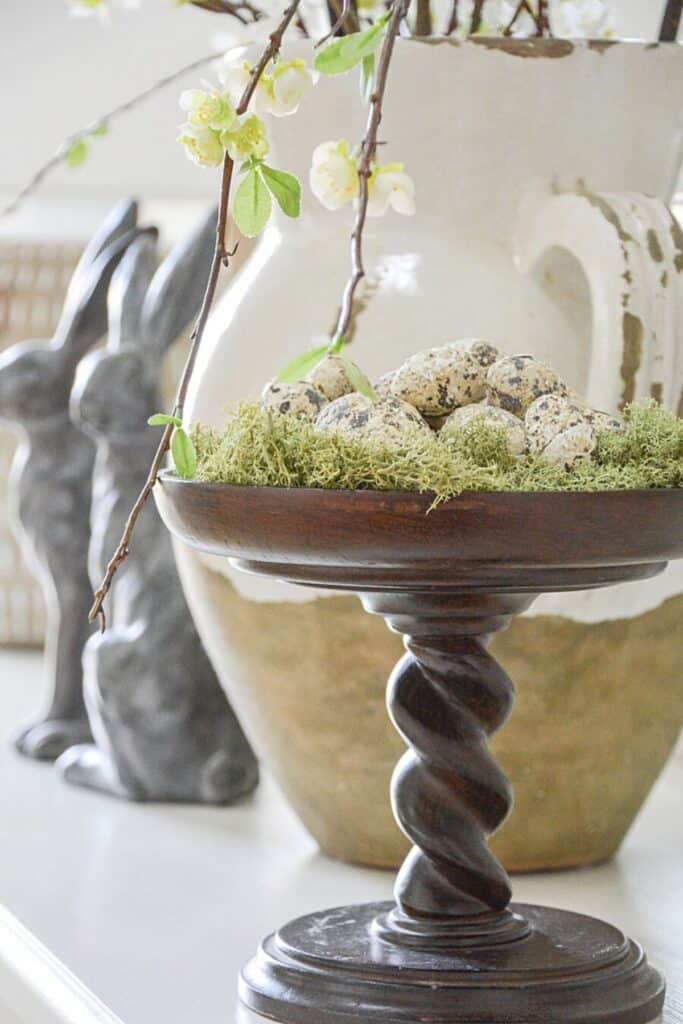 turned pedestal with moss and eggs and a pair of soapstone rabbits in the background