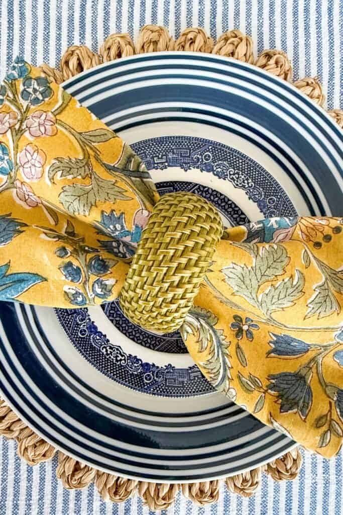 BLUE AND WHITE PLACE SETTING WITH A MUSTARD FLORAL NAPKIN AND A GREEN NAPKIN RING