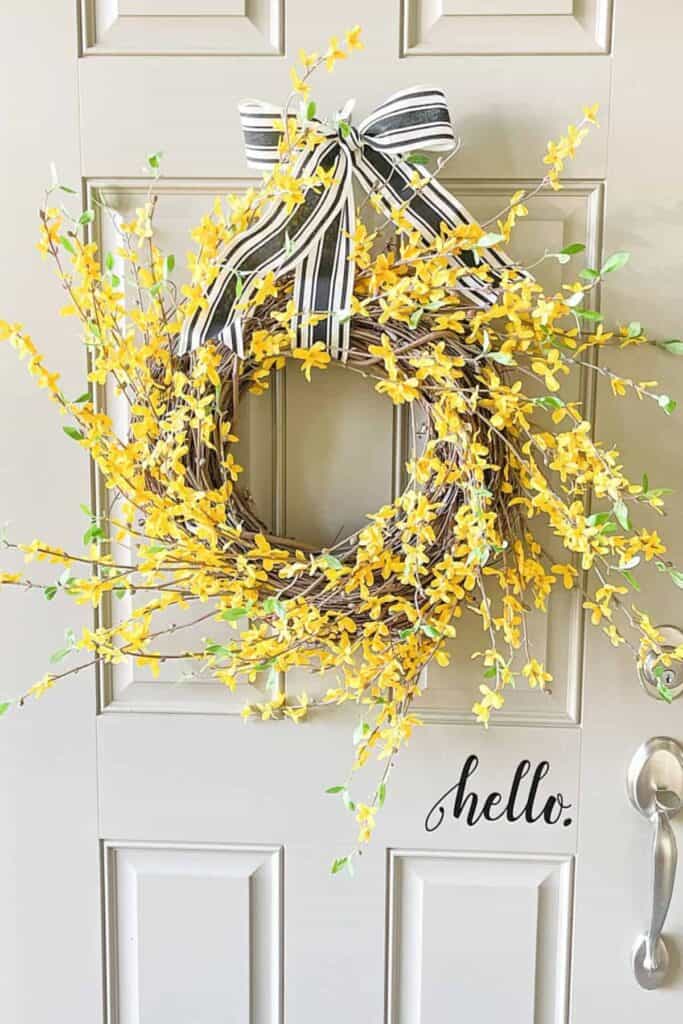 spring forsythia wreath hanging on a neutral front door with striped ribbon