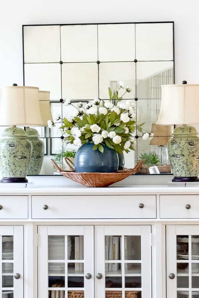 White buffet styled with two matching green lamps flanking a centered navy vase, showing balanced visual weight
