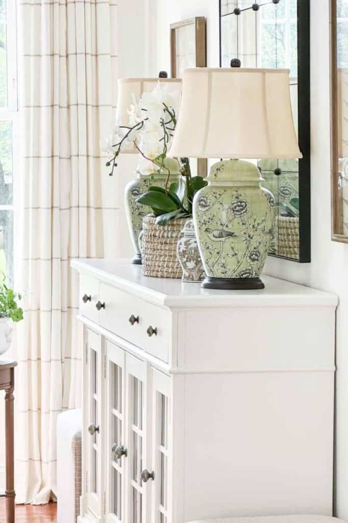 White buffet styled with green chinoiserie lamps and a white orchid, showing a tight color palette in a living room