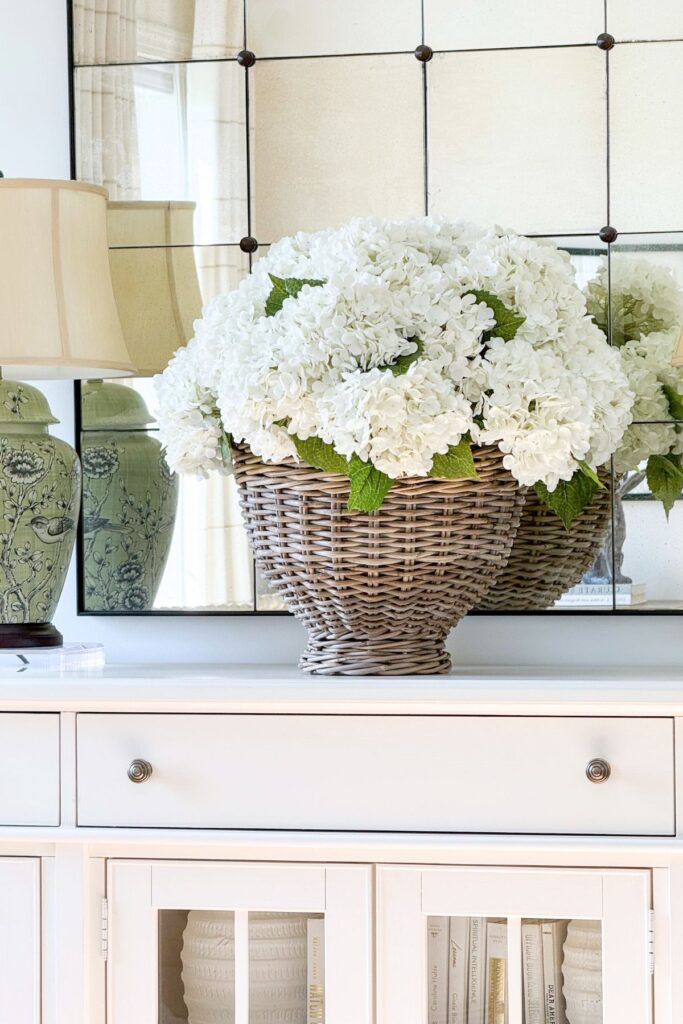 buffet styled with large hydrangea arrangement in basket, green lamps, and mirror for balanced home decorating