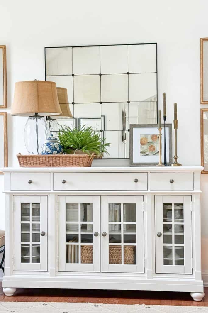 Framed citrus print leaned against a mirror on a white buffet with brass and black candlesticks of varying heights