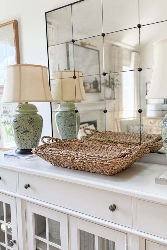 Low sided woven baskets on a white buffet flanked by green chinoiserie lamps