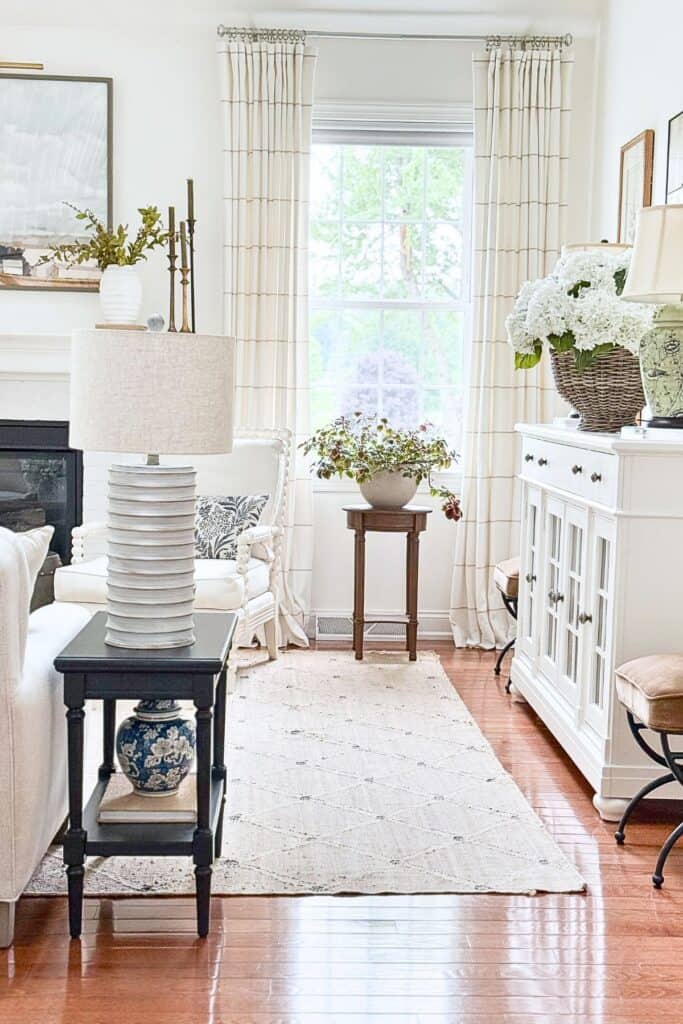 White buffet styled with a green lamp and floral basket, shown within a full neutral living room