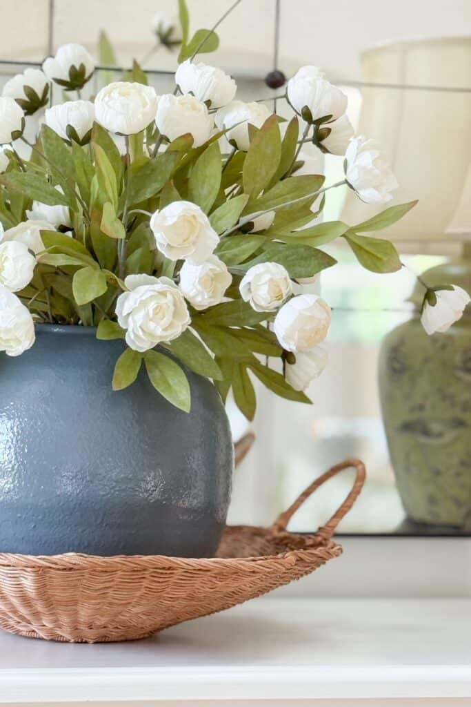 Close up of white florals in a navy vase with a woven basket, showing mixed texture on a buffet