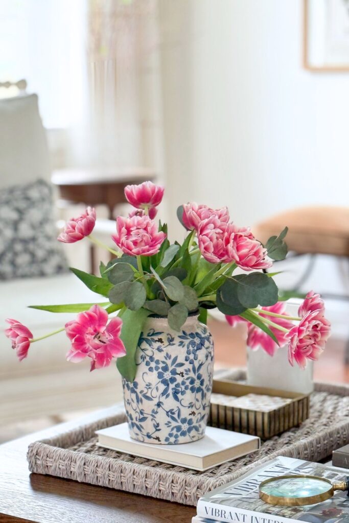 coffee table styled with blue and white vase, pink flowers, tray, books, and greenery for simple decorating ideas