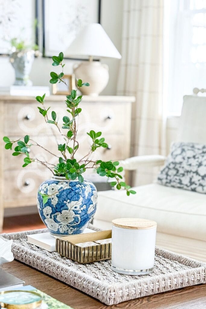 coffee table styled with woven tray blue and white vase greenery candle and decorative box in a bright living room