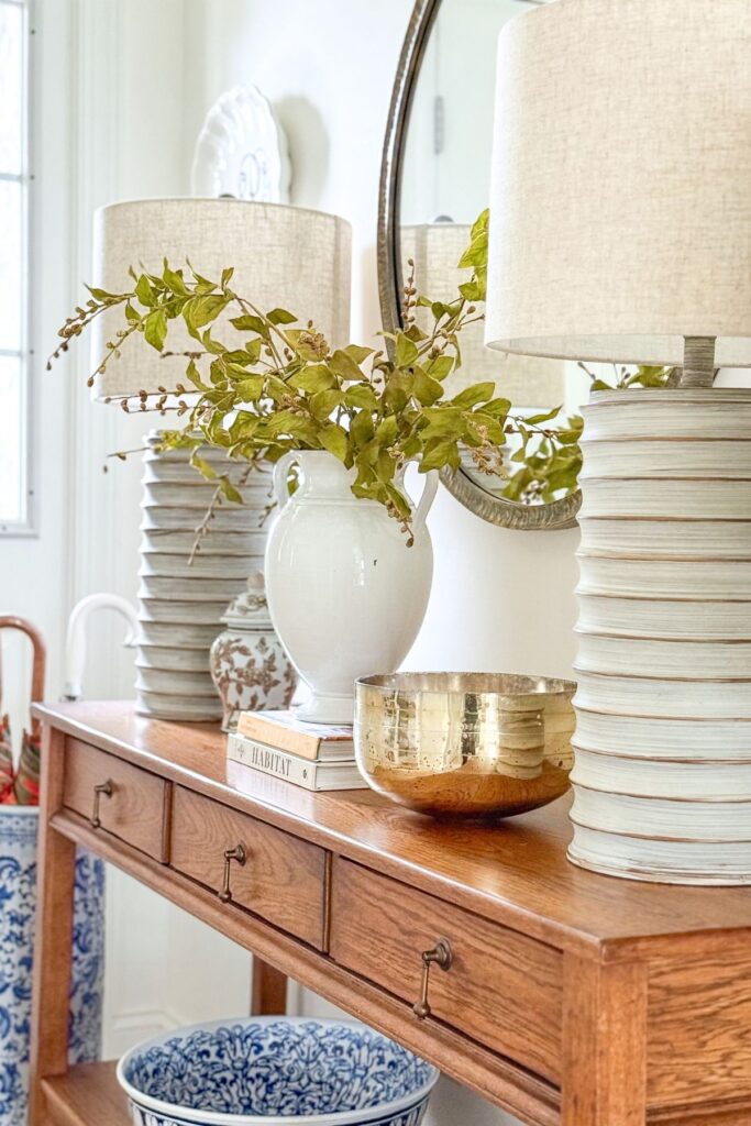 console table styled with lamp, white vase with greenery, stacked books, and decorative bowl for cohesive decorating