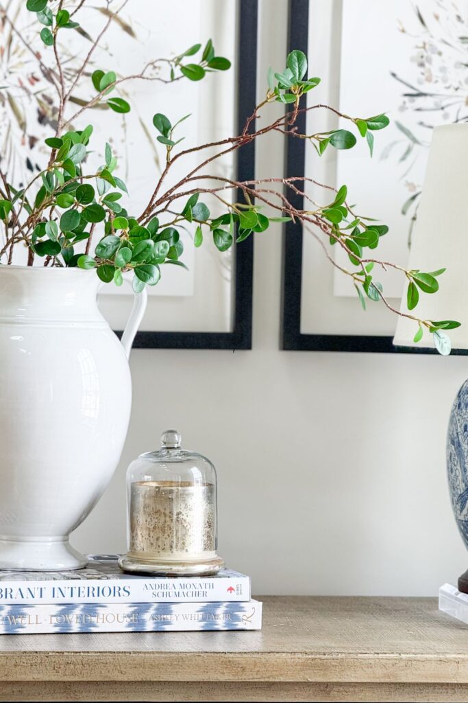 console table styled with white vase, greenery branches, stacked books, and blue and white decor for balanced decorating