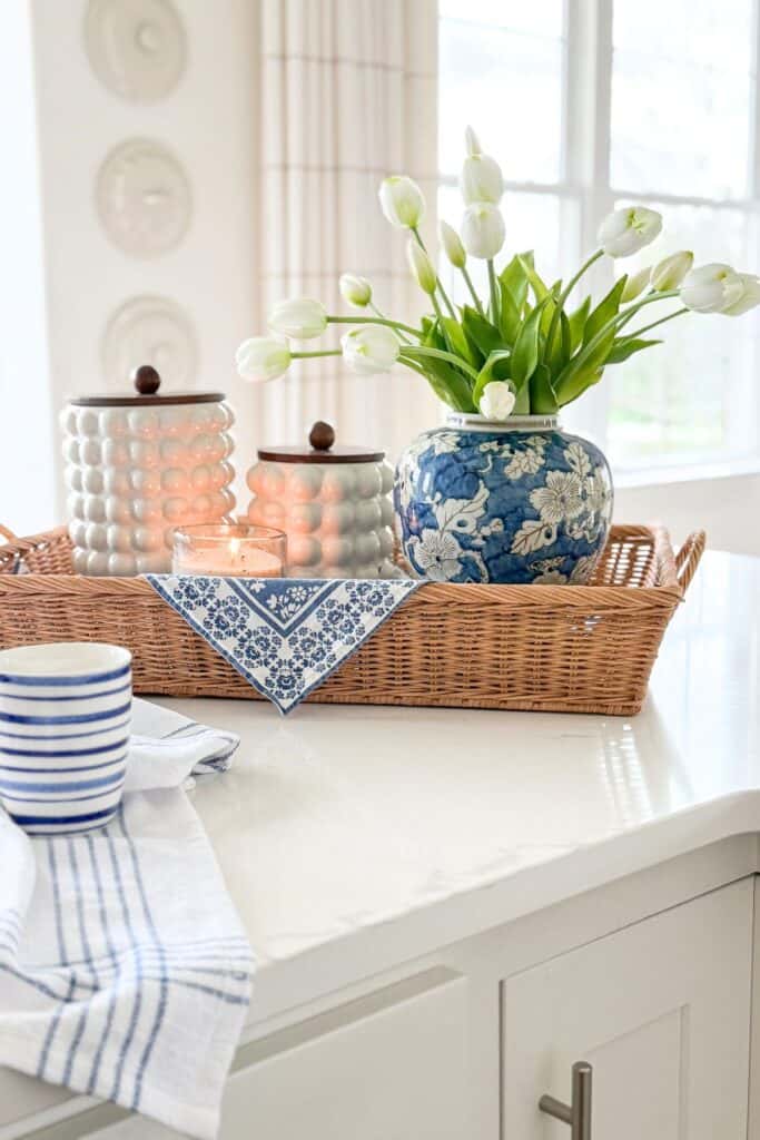 white tulips arranged in a patterned pitcher on a kitchen island tray with greenery and decor