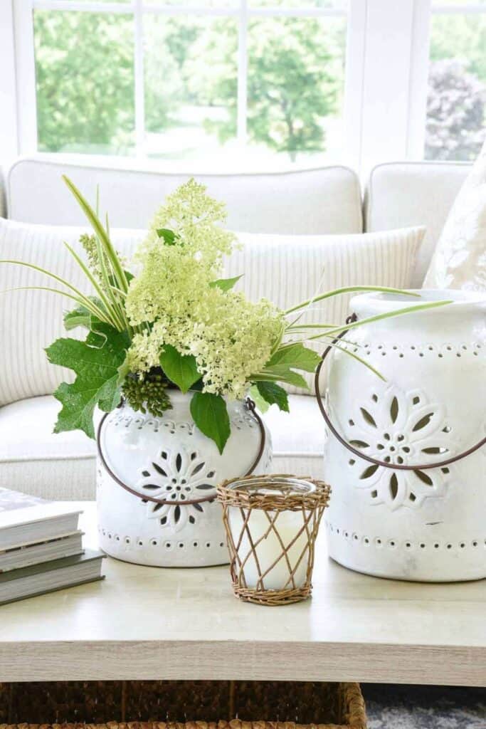 light green flowers and greenery arranged in a white container on a coffee table with neutral decor