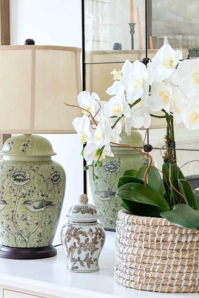 white orchid plant in a woven basket on a table with a lamp and decorative accessories