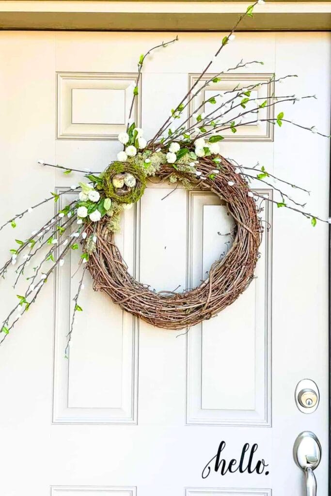 natural grapevine wreath with branches, greenery, and white flowers on a front door