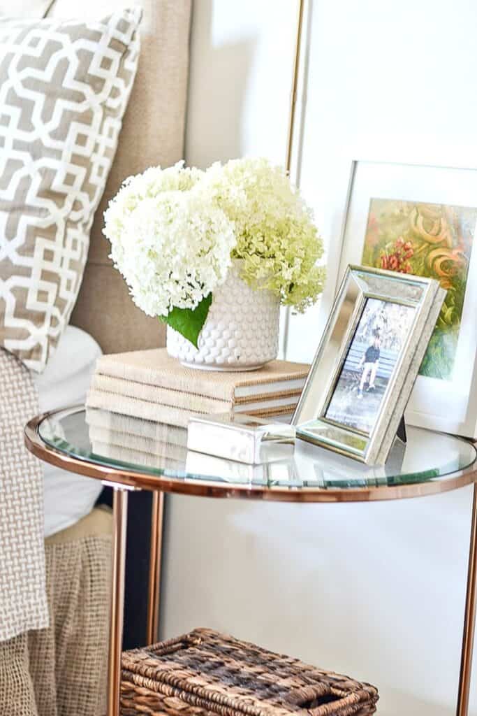 white hydrangeas in a small vase on a bedside table with books and framed photos