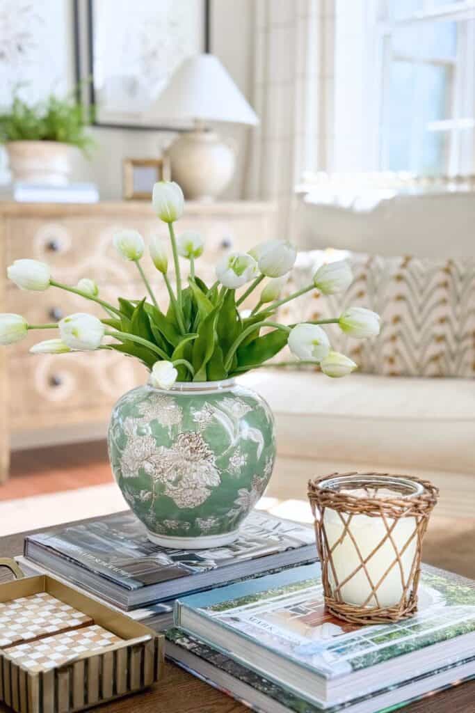 white tulips arranged in a green patterned vase on a coffee table with books and a candle