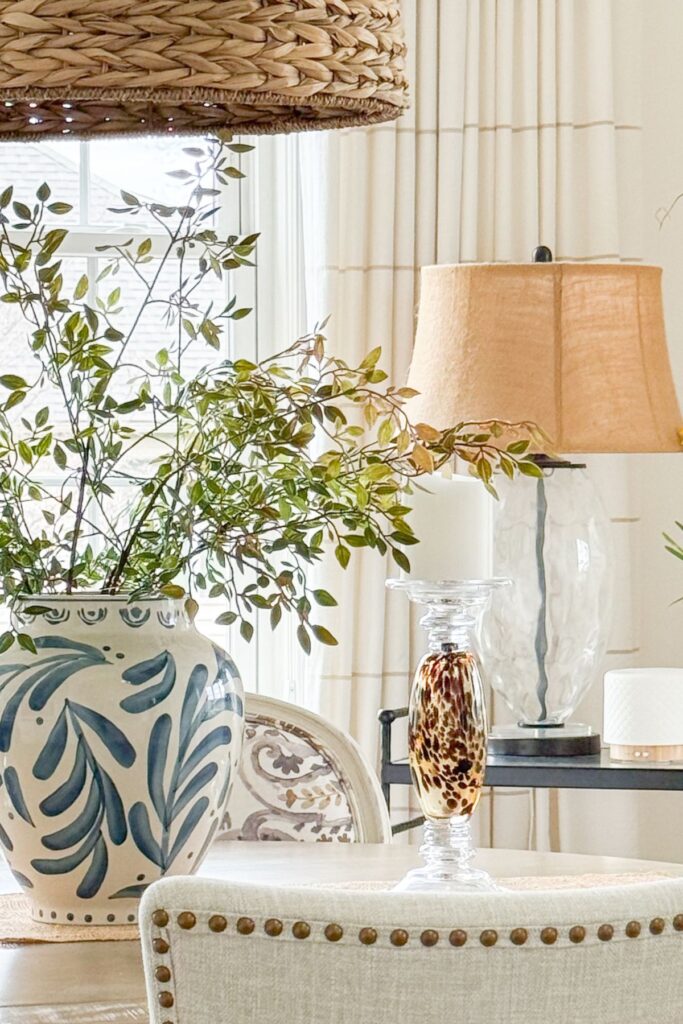 dining room table styled with blue and white vase, greenery branches, candle, and layered lighting for cohesive decorating