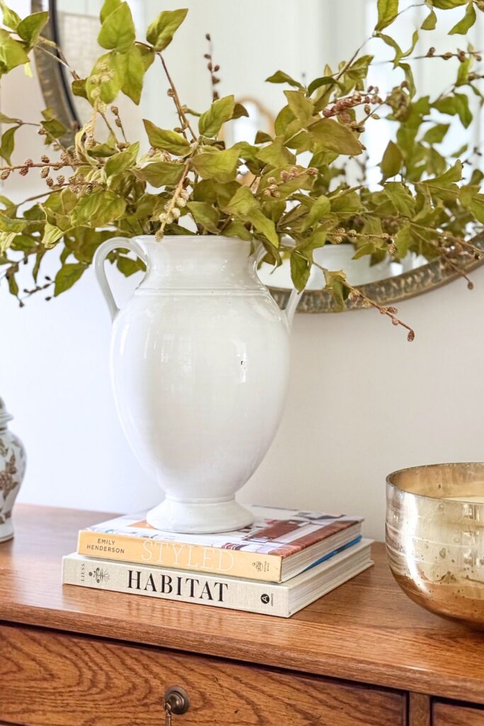dresser styled with white vase, greenery stems, stacked books, and candle for simple home decorating ideas