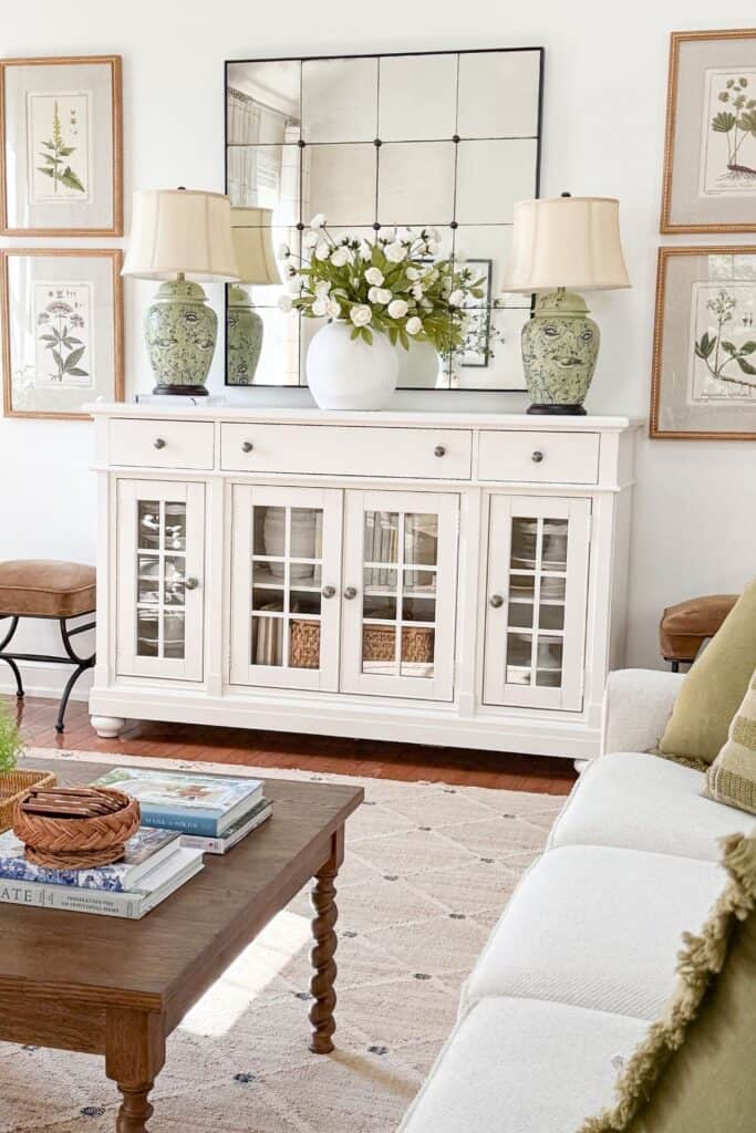 White buffet styled with a white vase of florals flanked by two green chinoiserie lamps in a living room
