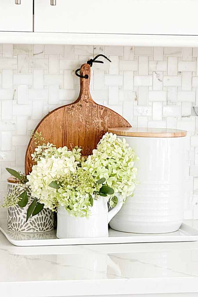 green hydrangeas arranged in a white pitcher on a kitchen counter tray with wood accents