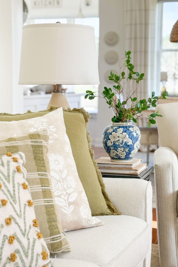 living room side table styled with blue and white vase, greenery, stacked books, and lamp for cohesive decorating