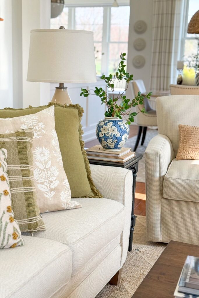 neutral living room styled with layered pillows, blue and white vase, greenery, and lamp for cohesive decorating