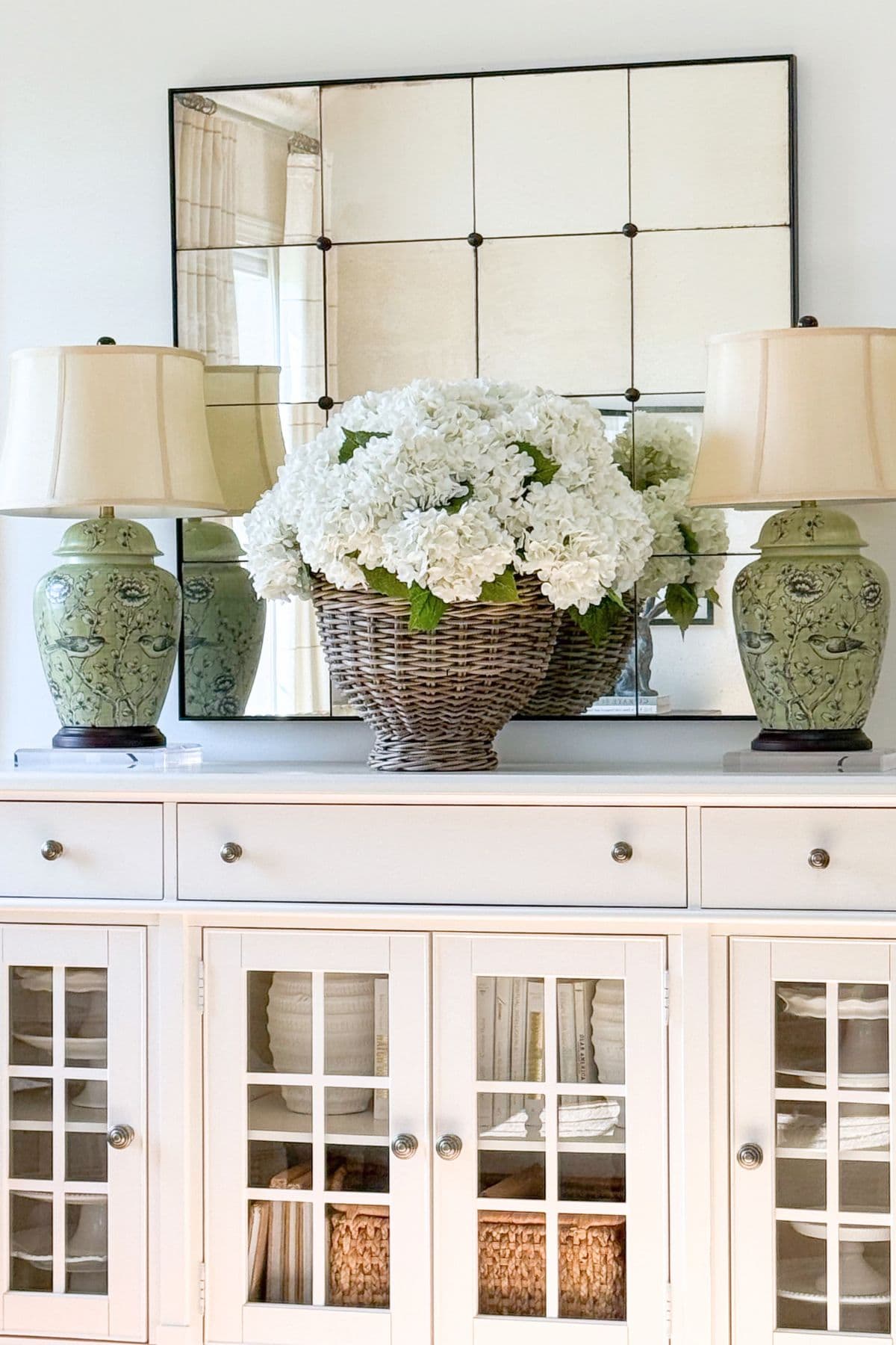 neutral buffet styled with white hydrangeas in a basket, green lamps, and a mirror for balanced home decorating