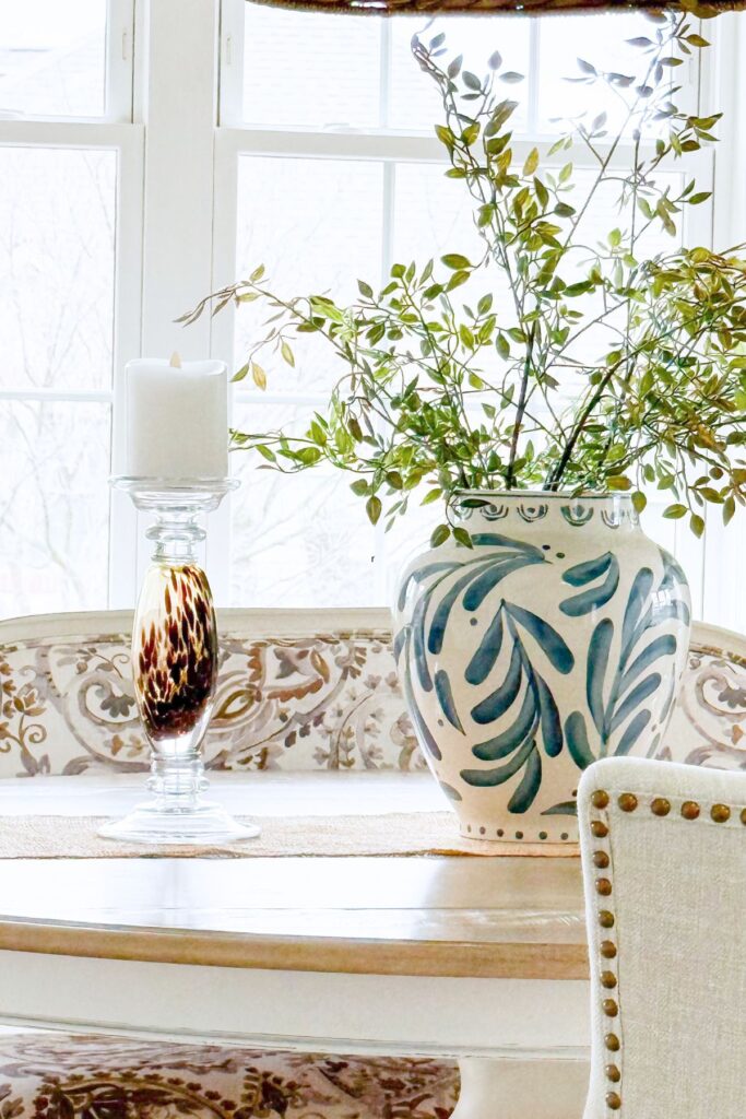 round dining table styled with blue and white vase, greenery branches, and candle for simple home decorating ideas