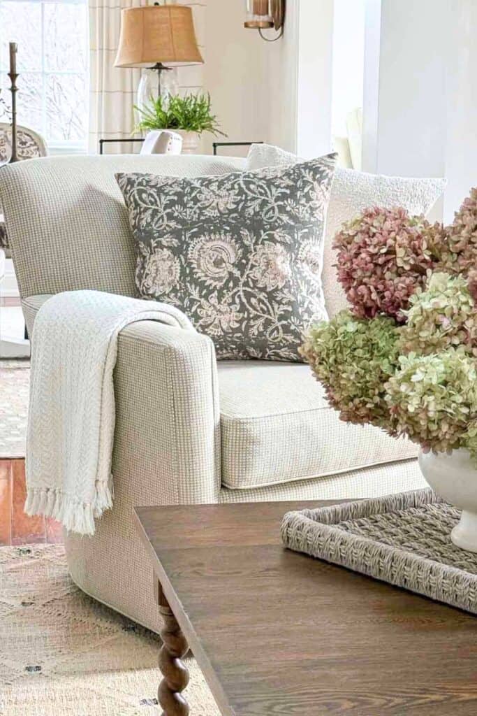 neutral living room chair styled with patterned pillow throw blanket and hydrangeas showing simple decorating ideas