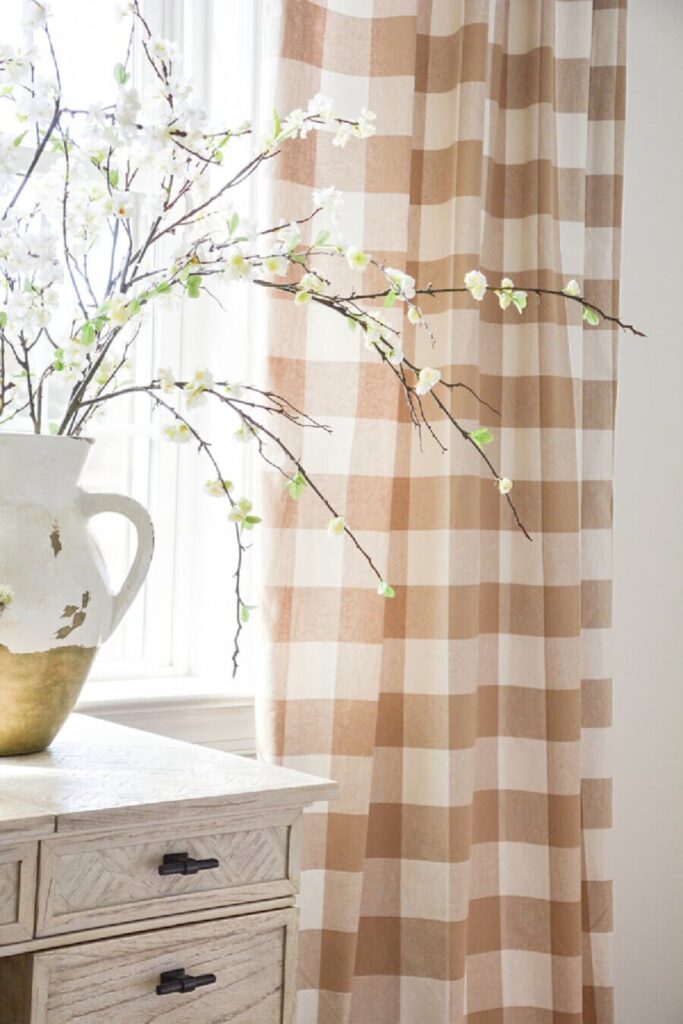 spring flowering branches in a white pitcher with neutral buffalo check curtains