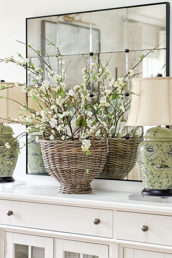 flowering branches arranged in a large woven basket on a sideboard with a mirror behind