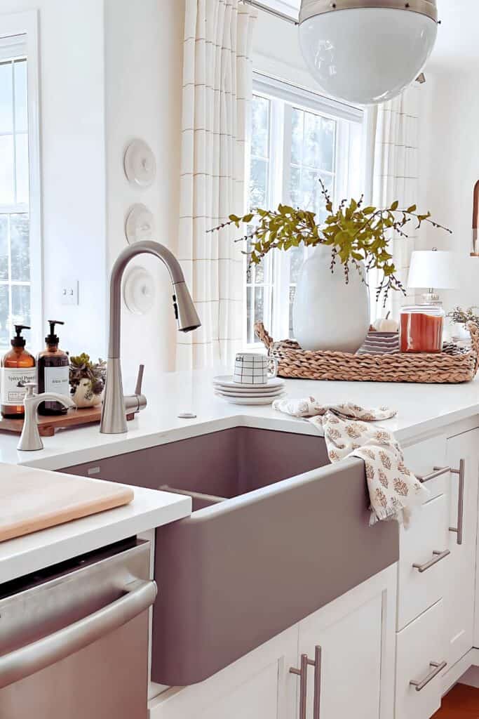 Kitchen countertop focal point with a fall vignette of a ceramic vase, woven tray, and linen napkin by the sink
