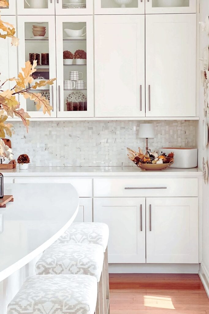 Kitchen countertop fall decor with a bowl of pumpkins and gourds beneath a branch of golden leaves