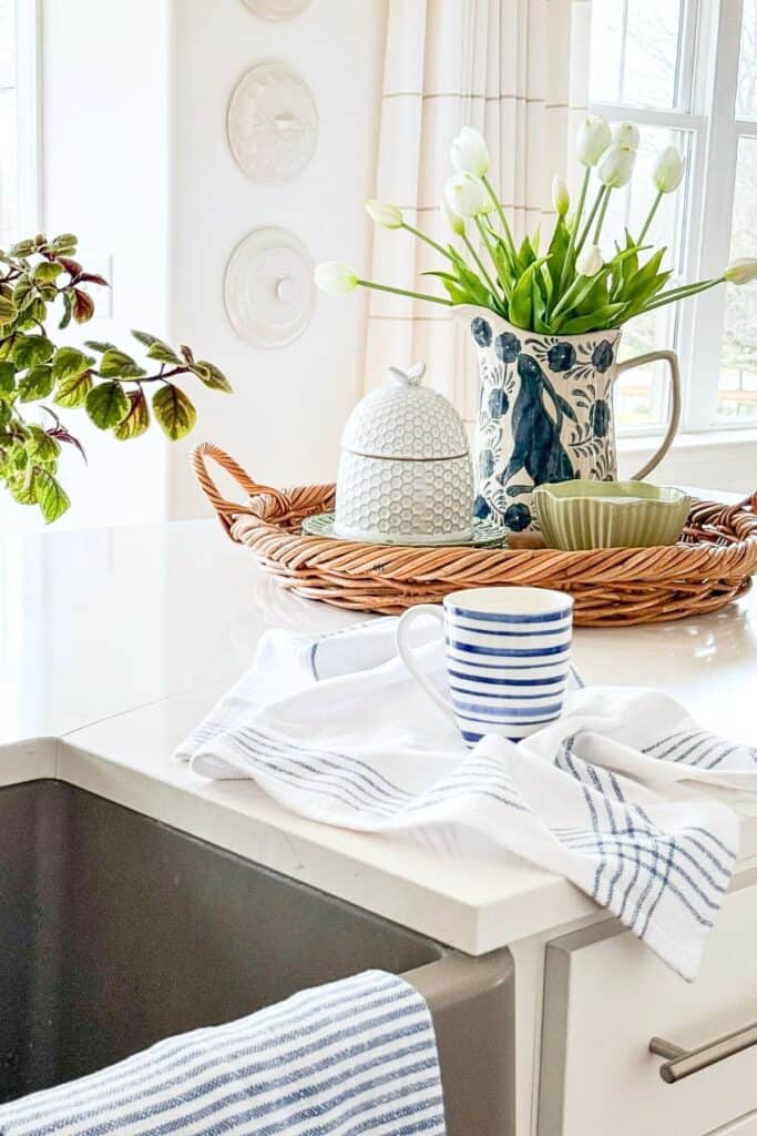 Kitchen countertop focal point with a spring vignette of tulips, a honeycomb jar, and striped mugs on a woven tray