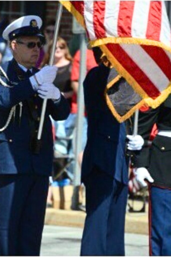 Military color guard in dress uniforms carrying the American flag with white gloves during a Memorial Day parade