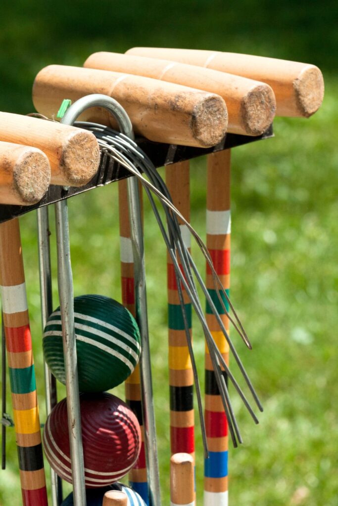 Vintage wooden croquet mallets and colorful striped balls on a rack in green grass ready for backyard lawn games on Memorial Day weekend