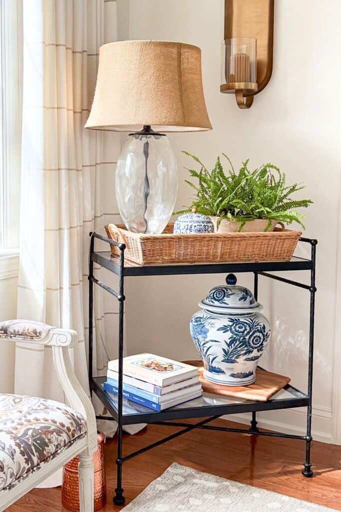 black iron and glass bar cart styled with a traditional glass lamp, blue and white ginger jars, and a fern in a woven basket