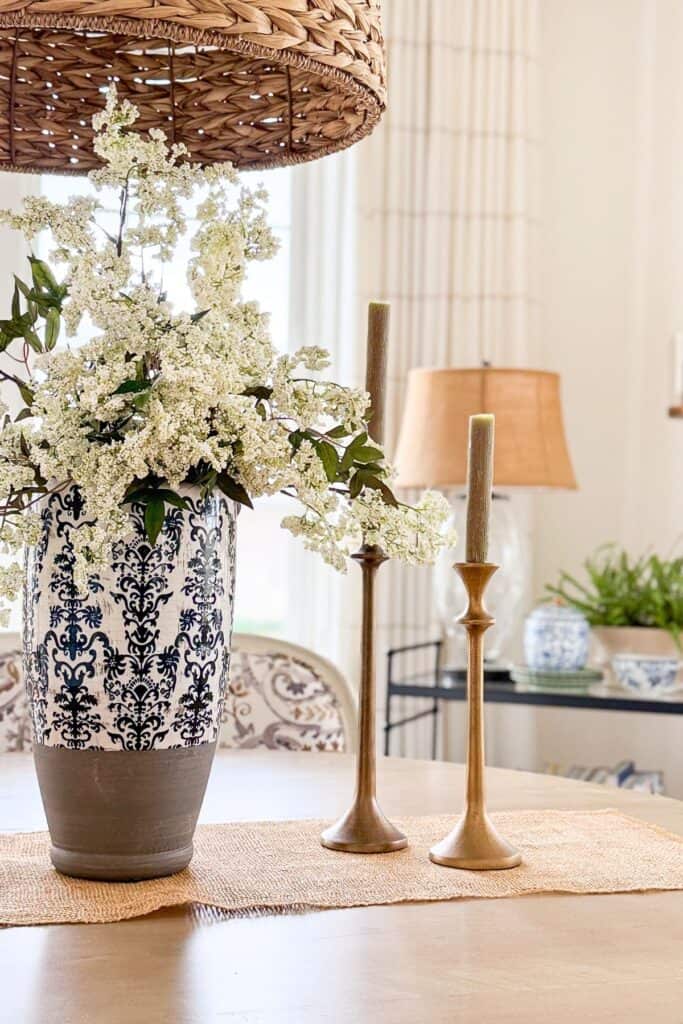 blue and white damask vase with white flowering branches next to modern gold taper candlesticks on a wood table