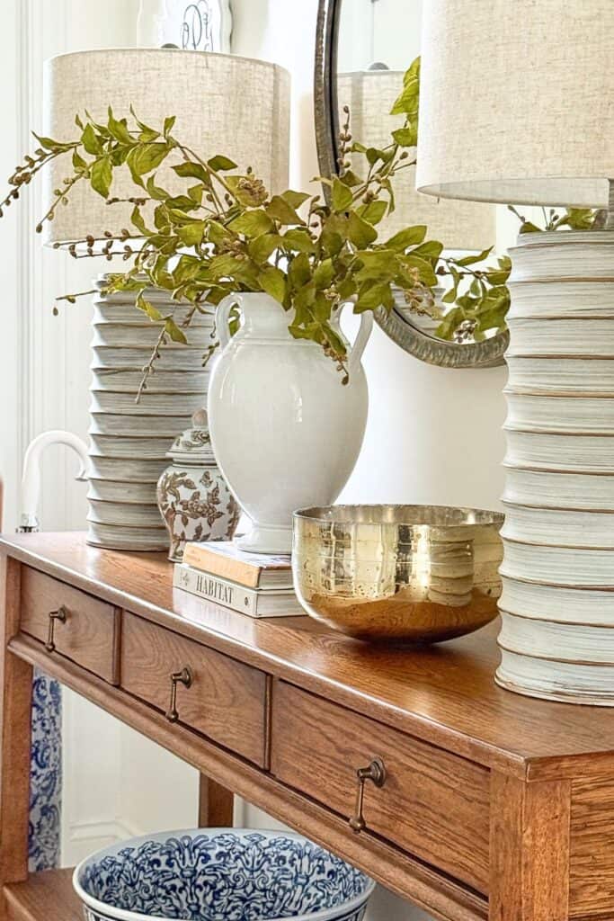 classic wood console table styled with a chinoiserie ginger jar, white pitcher, gold mercury glass bowl, and ribbed ceramic lamps